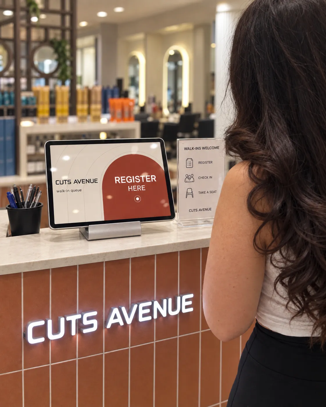 A customer at the Cuts Avenue front counter, beside the walk-in check-in screen.